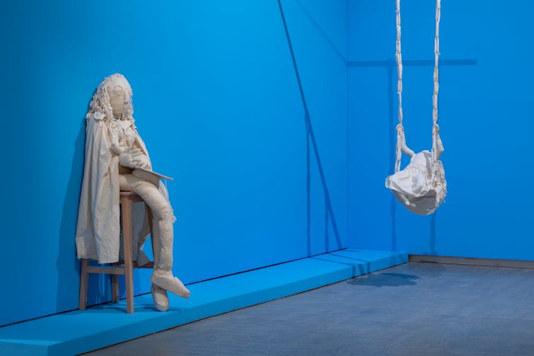 Two sculptures of white fabric in a blue gallery.