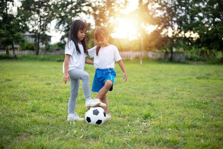 Two girls play soccer in the park.