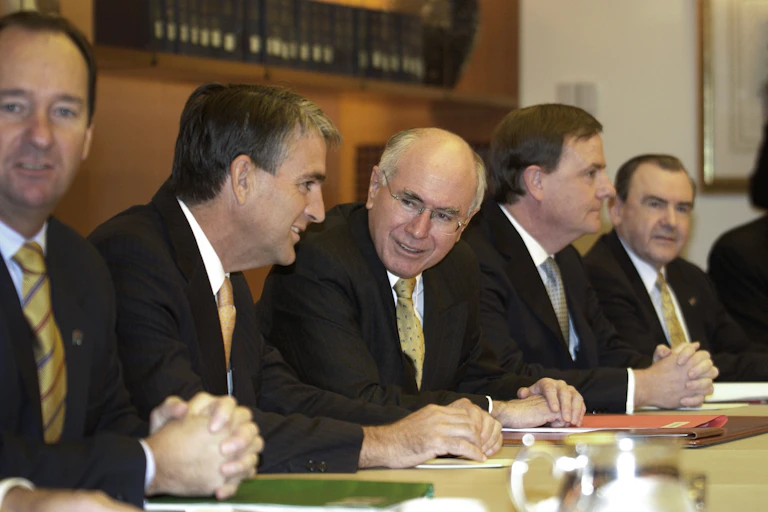 Senior members of the Howard cabinet, along with PM John Howard, are clustered around a table.