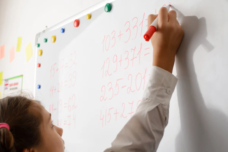 A girls writes sums on a whiteboard.