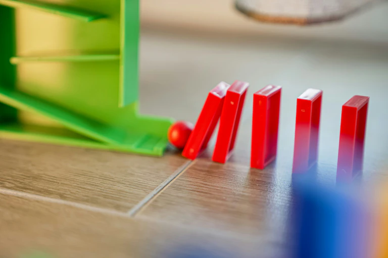 Close-up of a stack of bright red dominoes being knocked over on a table.