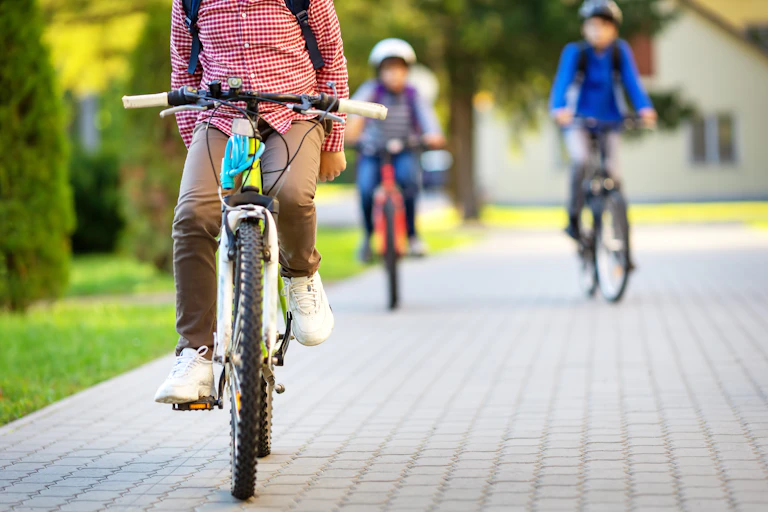 man on bike, two kids on bikes behind with school rucksacks and helmets on