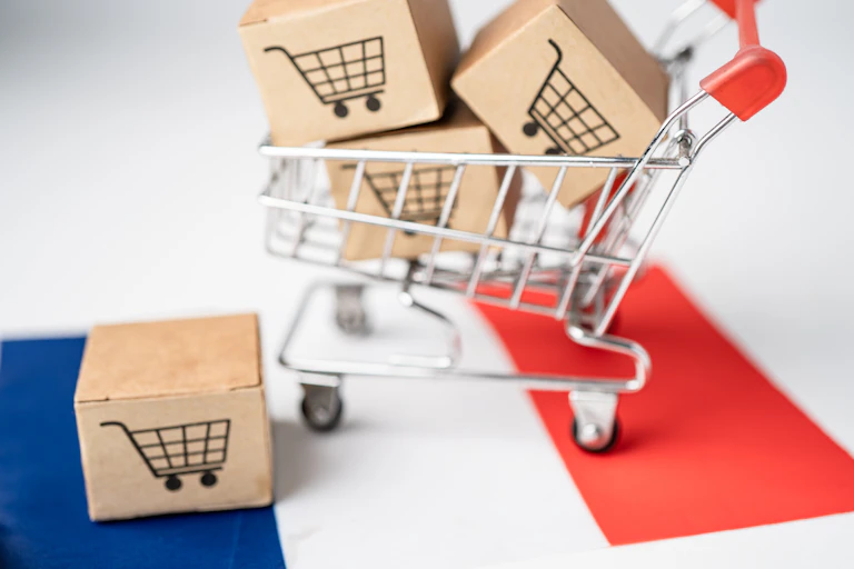 un chariot de magasin rempli avec des cartons posé sur un drapeau bleu blanc rouge