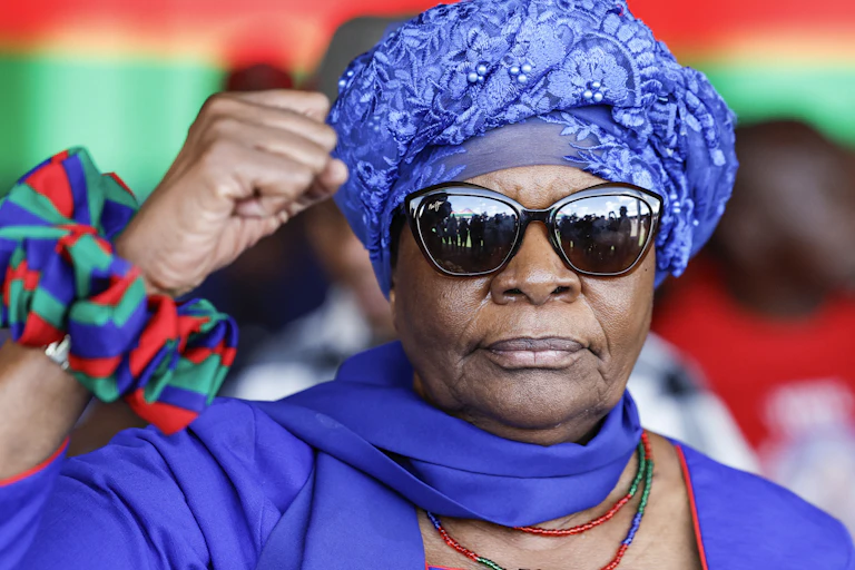 A woman wearing a turban and sunglasses raises her right hand in a black power salute