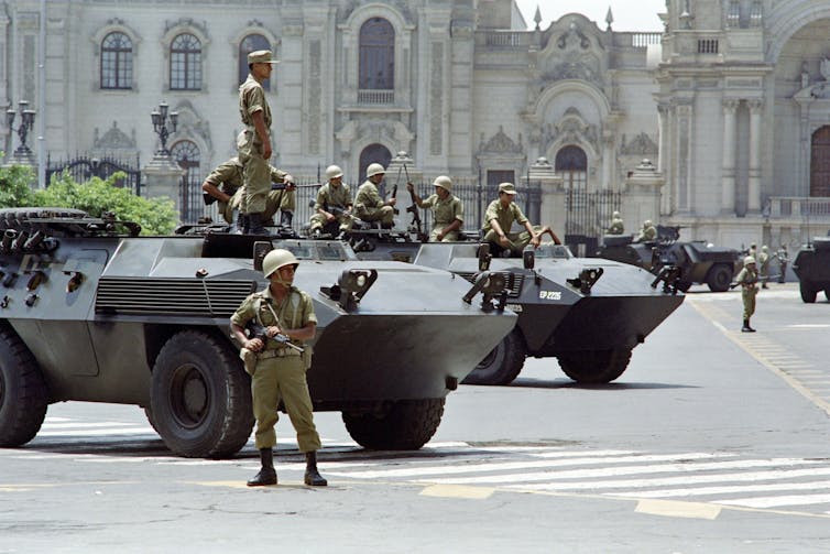 Men holding guns stand next to and on tanks.