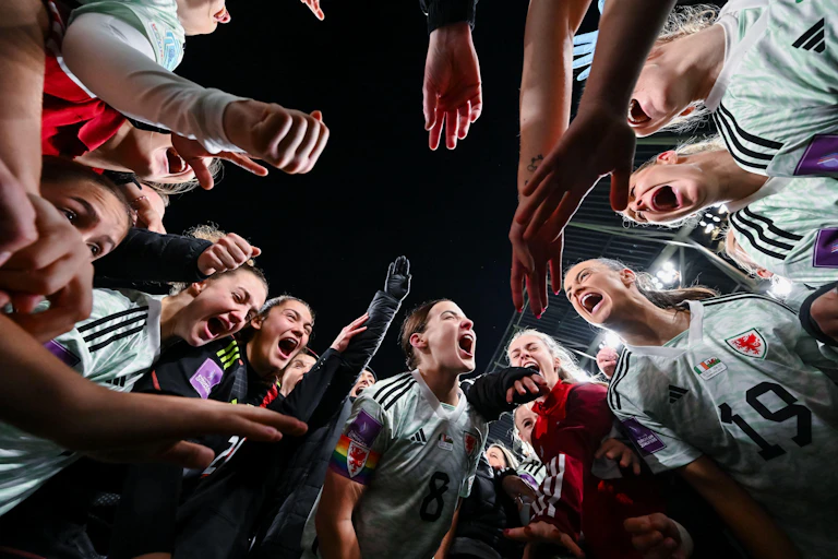 A group of women footballers celebrate in a circle.