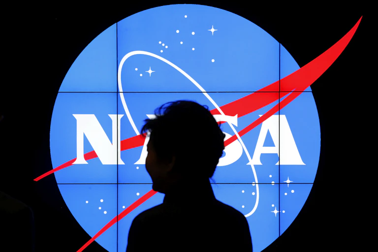 A figure silhouetted against a lit up NASA logo