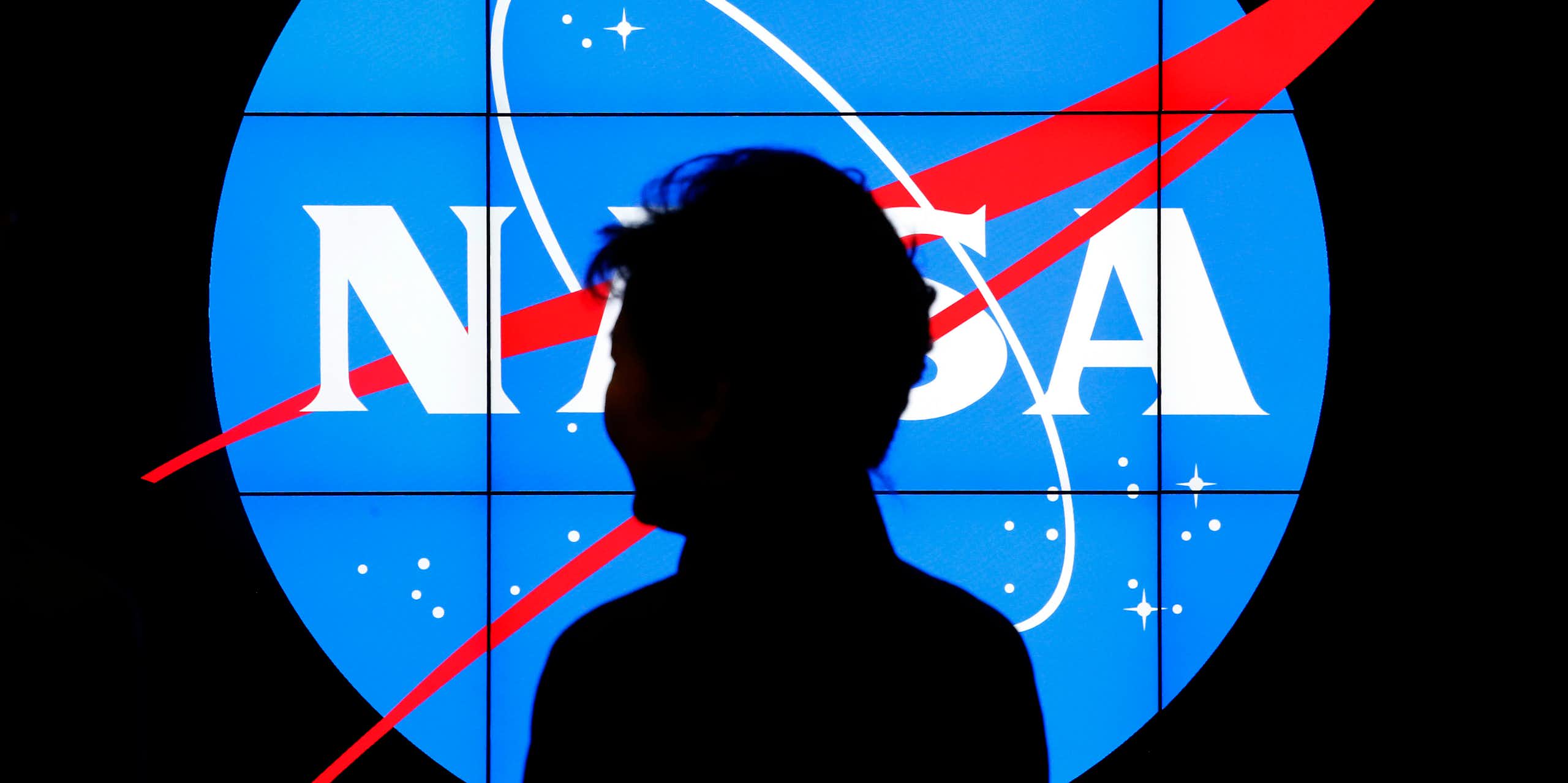 A figure silhouetted against a lit up NASA logo