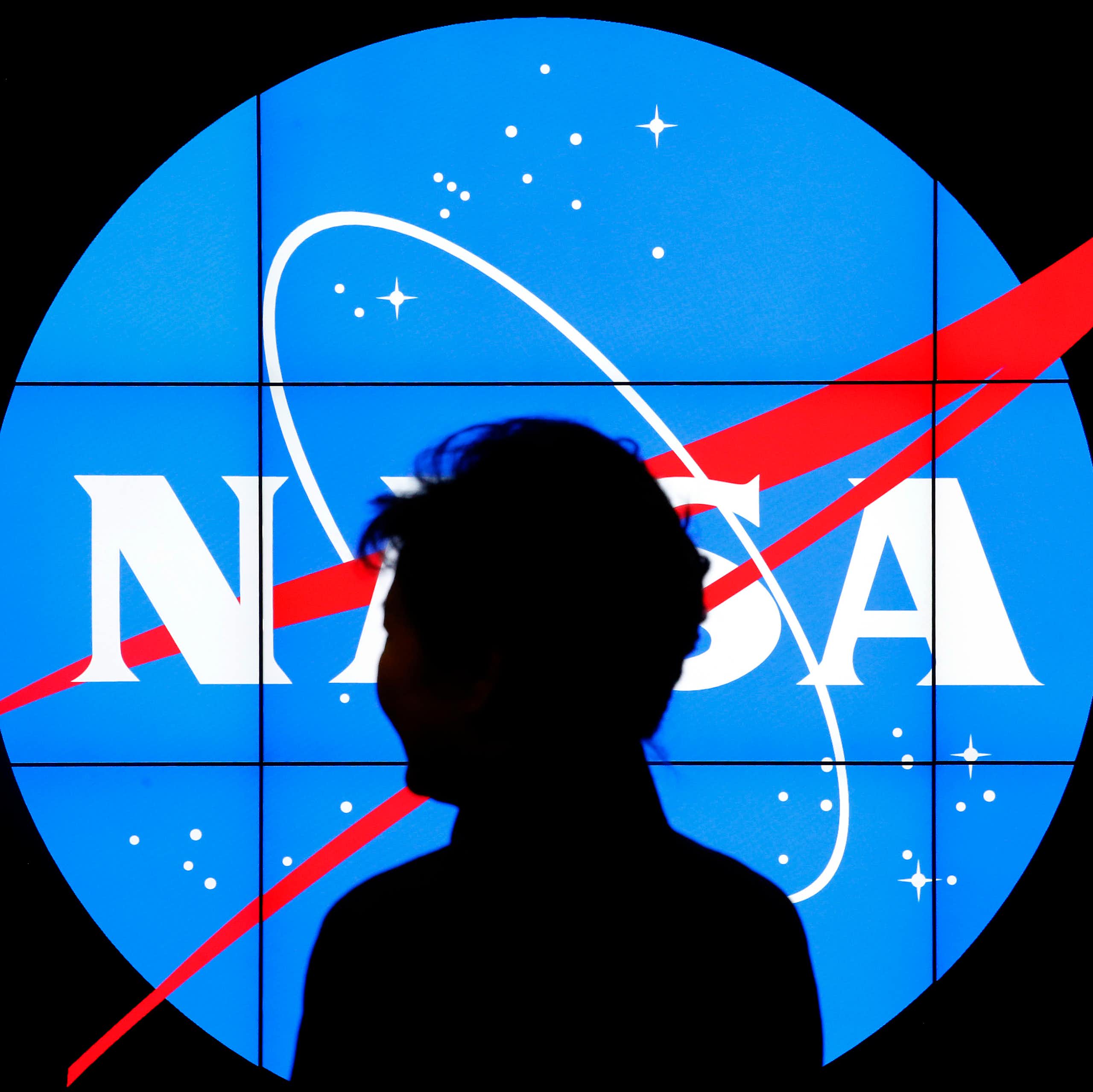 A figure silhouetted against a lit up NASA logo