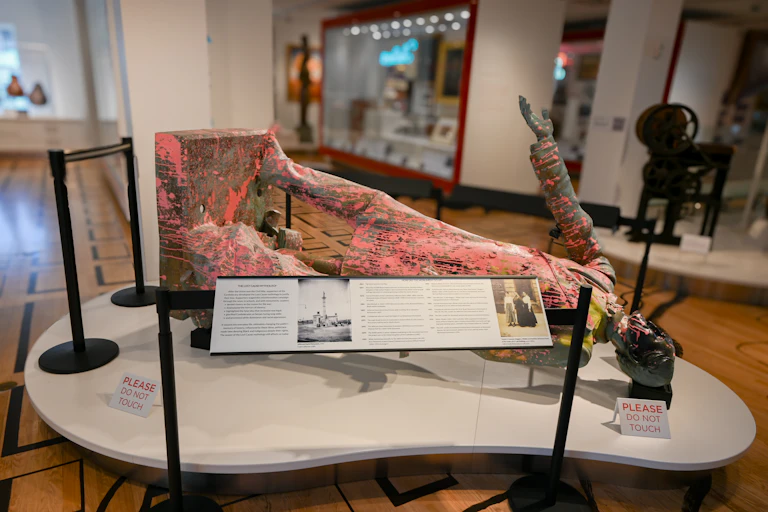 Pink paint-spattered bronze statue lies on its back on a display table