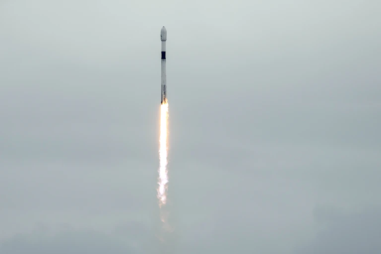 A long cylindrical rocket shooting upwards, with a plume of flame trailing it.