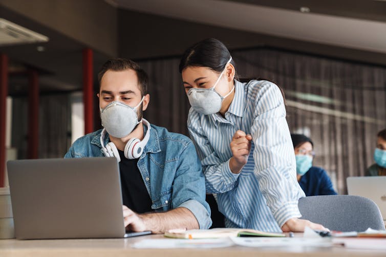 Two students wearing face masks looking at a laptop