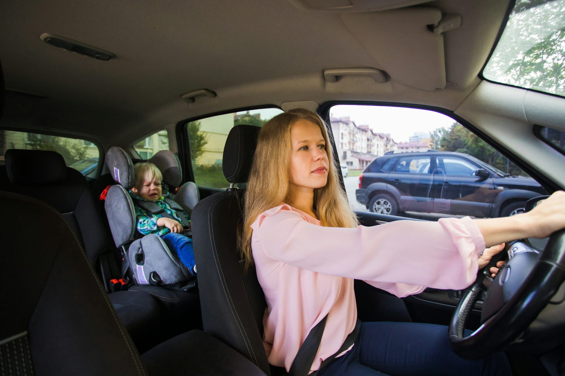 A woman drives a car while her child cries in the back.