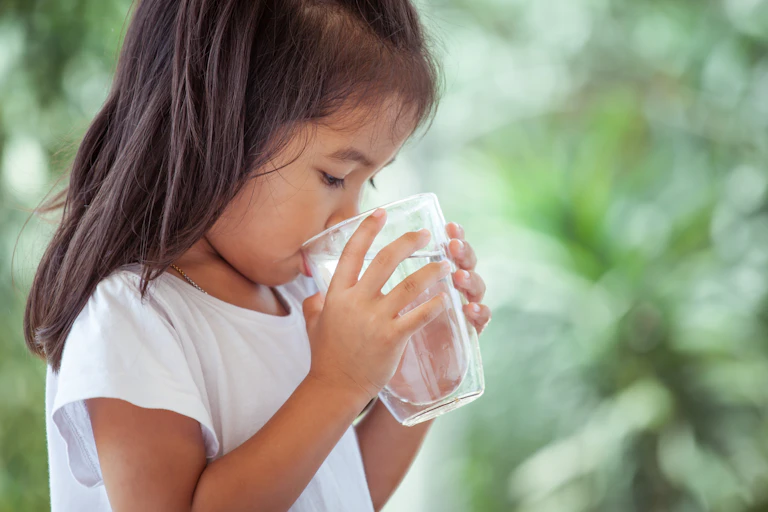 A young girl drinks a glass of water.