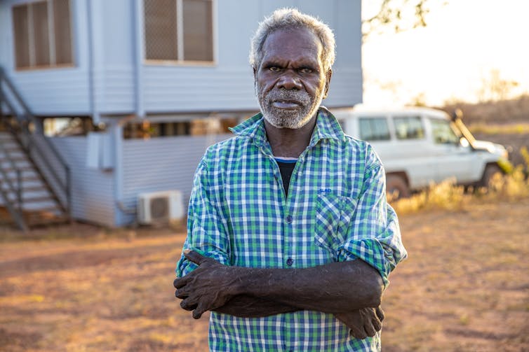 older aboriginal man poses in front of house