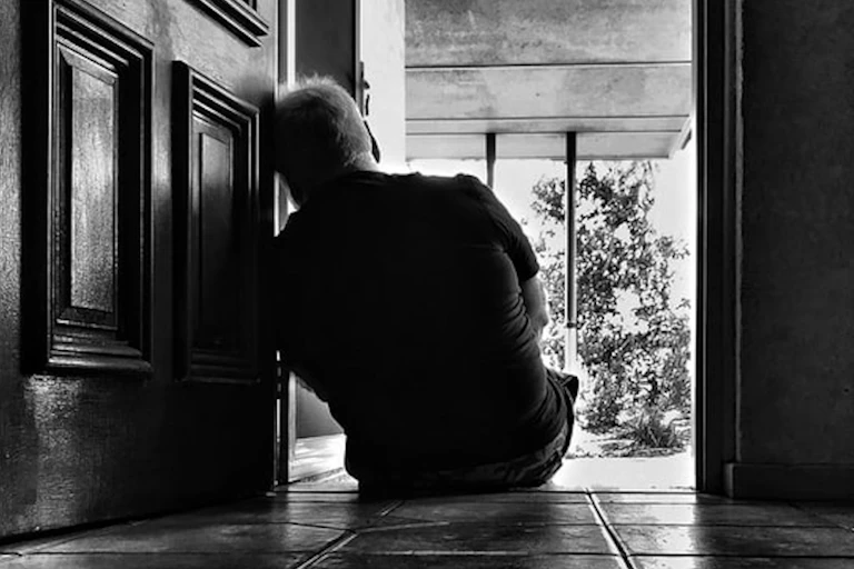 Black and white photo, the back of a man sitting in a doorframe.