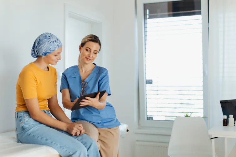 A nurse talks to a patient sitting on a bed.