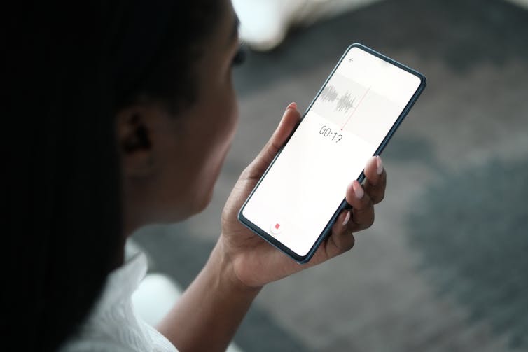 A woman holds a smart phone recording a voice memo.