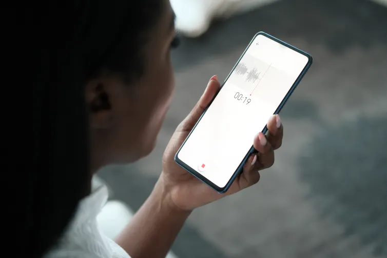 A woman holds a smartphone recording a voice memo.