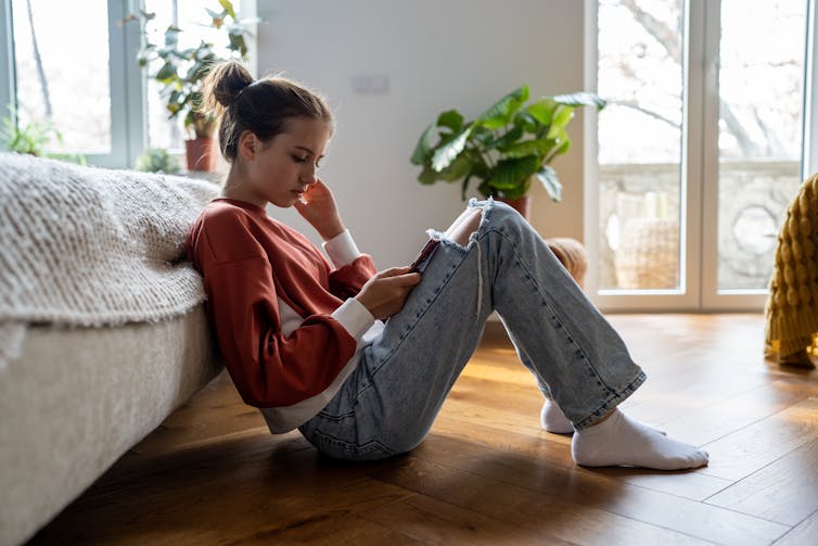 A teen girl sitting down using her phone.