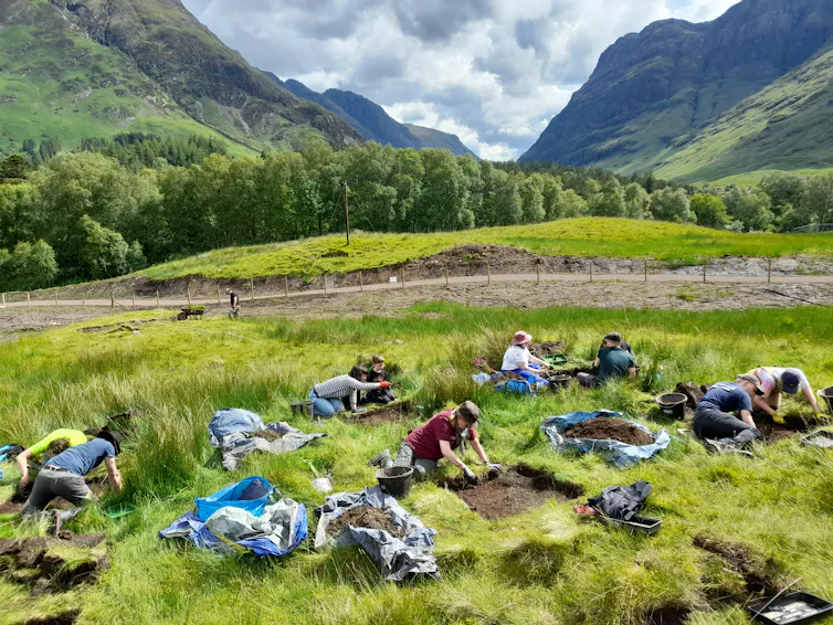 A group of archaelogists on their hands and knees excavating artefacts.
