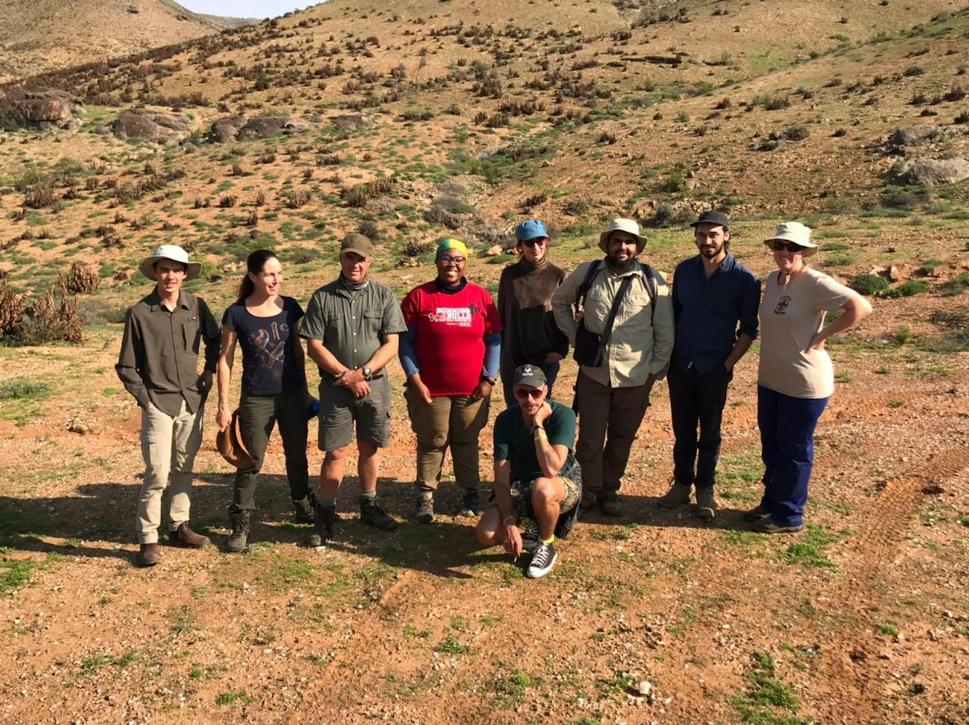 A group of nine people standing outdoors in a desert like area