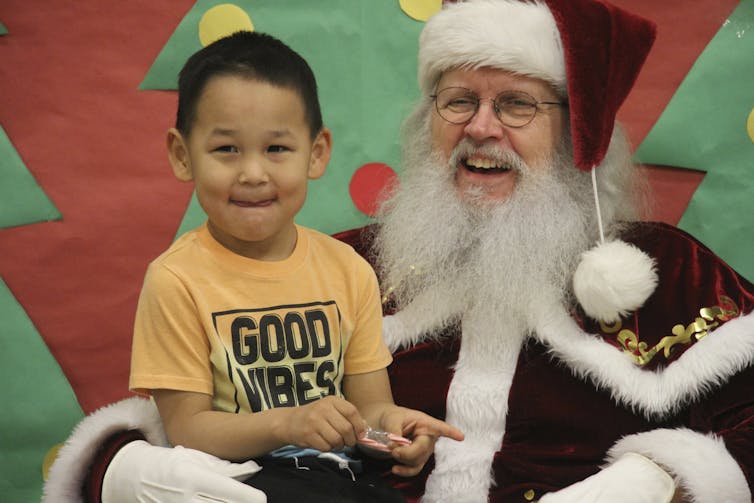 Santa Claus with a child in his lap; both are smiling.