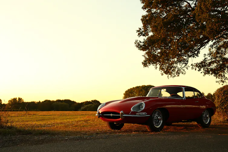 Red Jaguar E-type parked in a field.