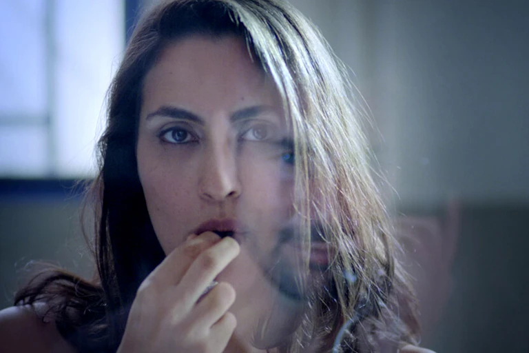 a woman looks directly into the camera as she puts a candy into her mouth.