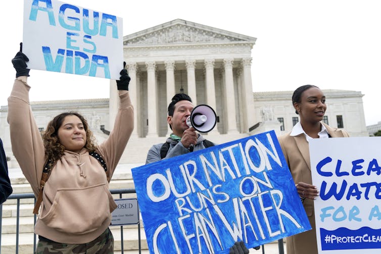 People holding signs stand outside a marble building with pillars.