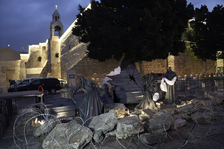barbed wire surrounding rocks and statues of people caring white shrouds.