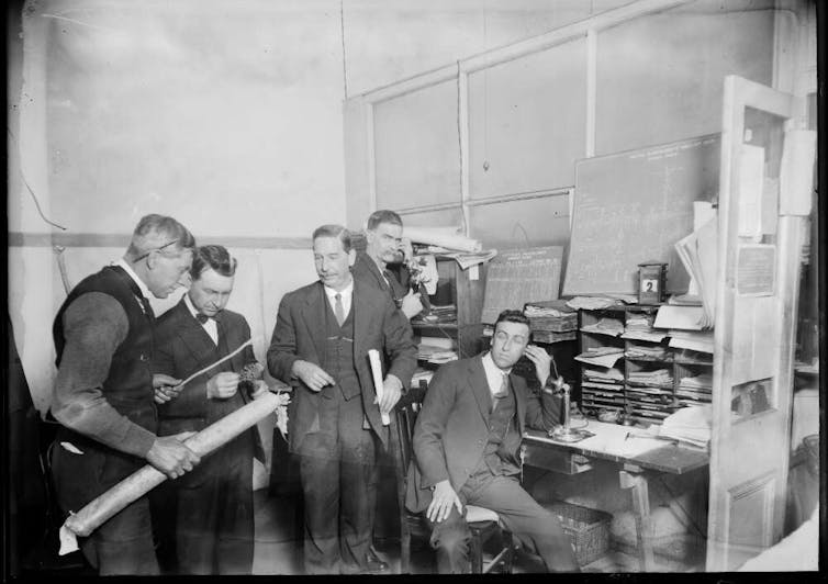 Men in suits answer phones in an office.