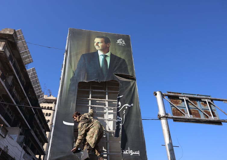A man tearing down a portrait of Bashar al-Assad on a building.