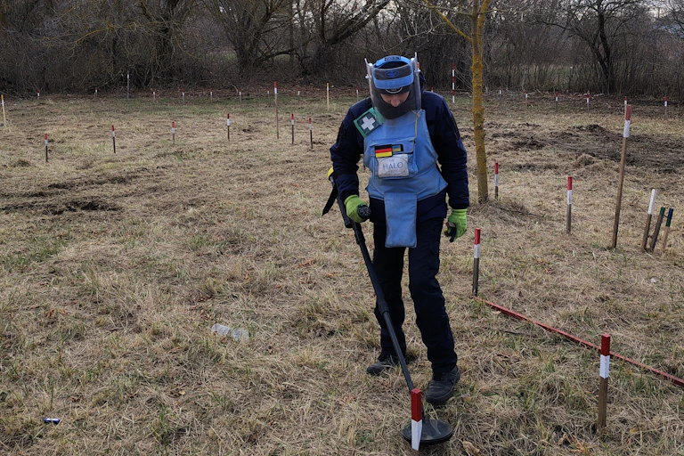 A man in a blue uniform wielding a metal detector.