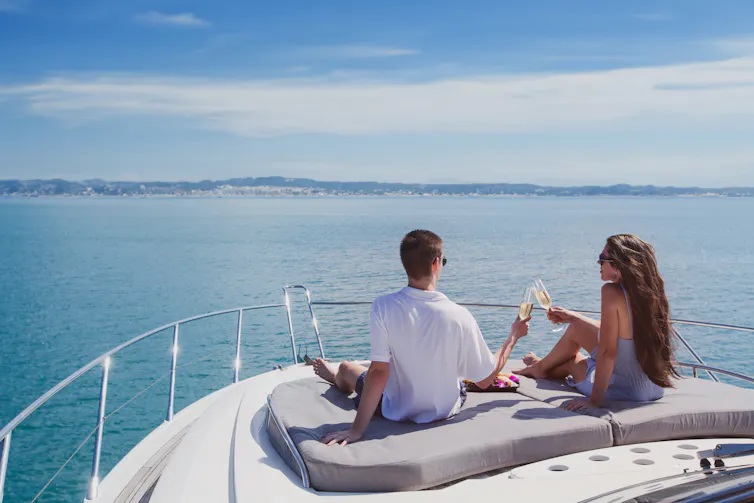 A couple clink champagne glasses while sitting at the front of a luxury yacht.