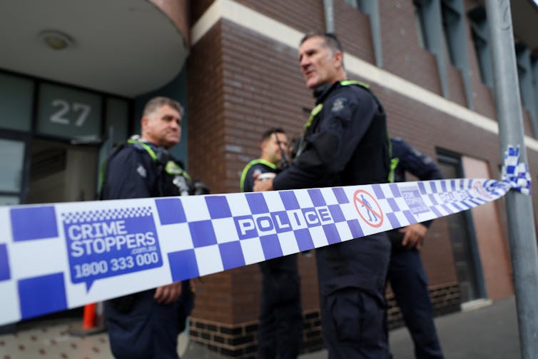 A group of male police officers stand behind police tape