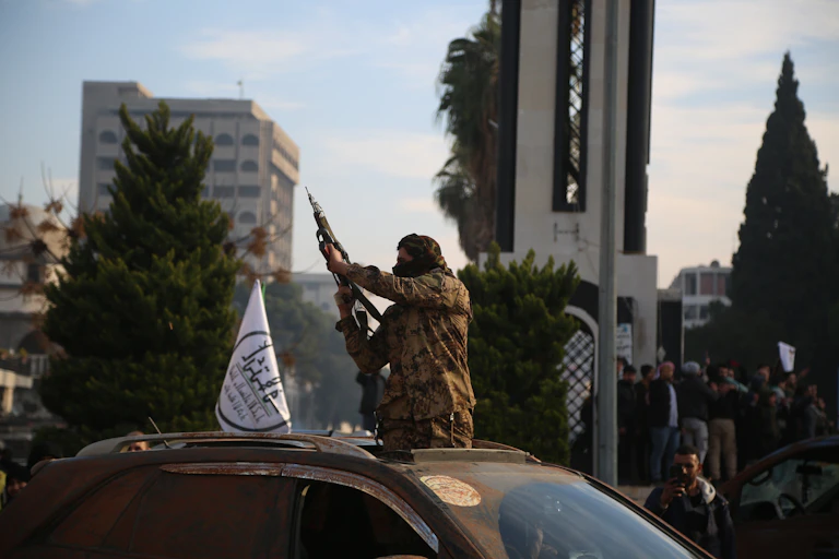 A Syrian rebel holding a gun aloft through the roof of a car.