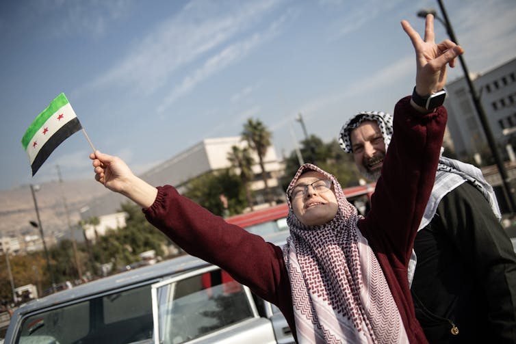 A Syrian woman celebrating with her arms aloft and holding the Syrian opposition flag.