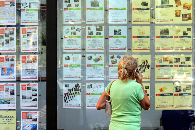A woman wearing a green T-shirt standing in front of the storefront of an Italian real estate agency.