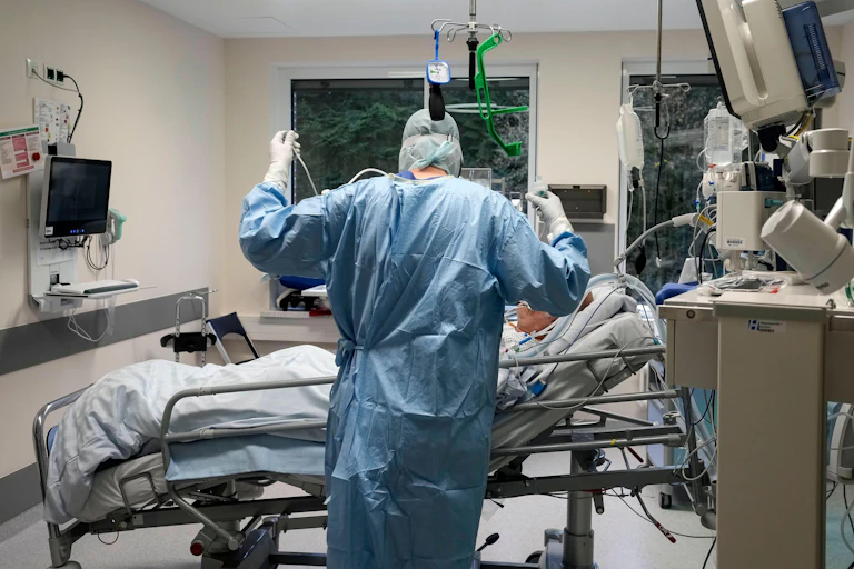 A doctor stands in front of an intubated patient in an ICU.