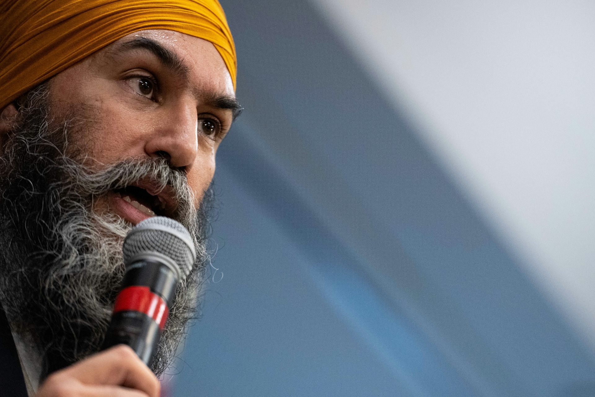 A man in an orange turban and a grey beard speaks into a microphone.