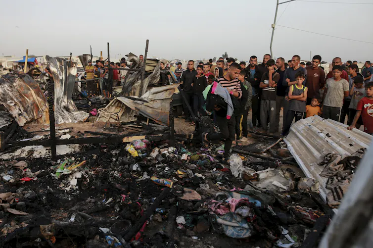 Charred remains of housing with a crowd of people looking on