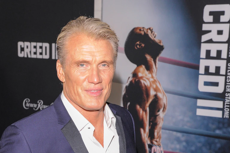 Dolph Lundgren wearing suit in front of Creed II poster