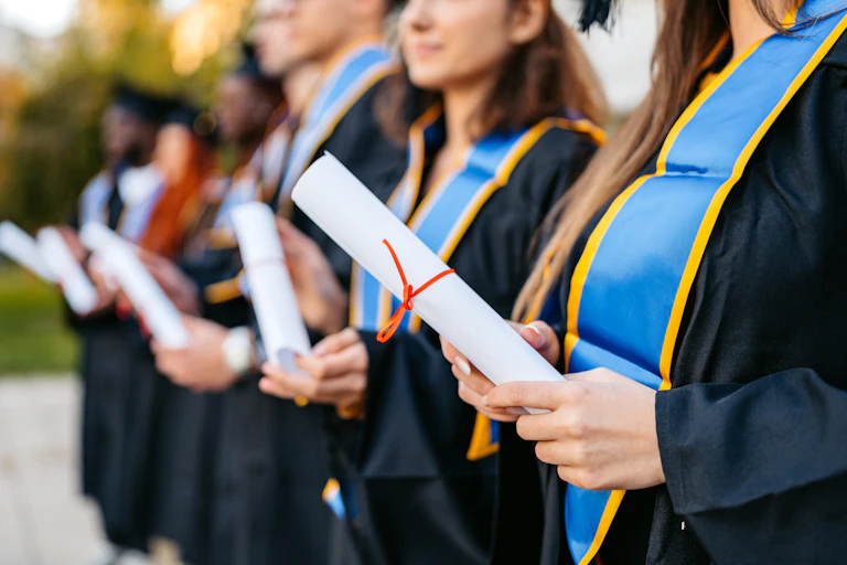 men and women wearing graduation gowns with blue sashes hold diplomas