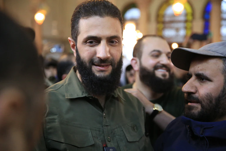 A man with a beard talks to others people.