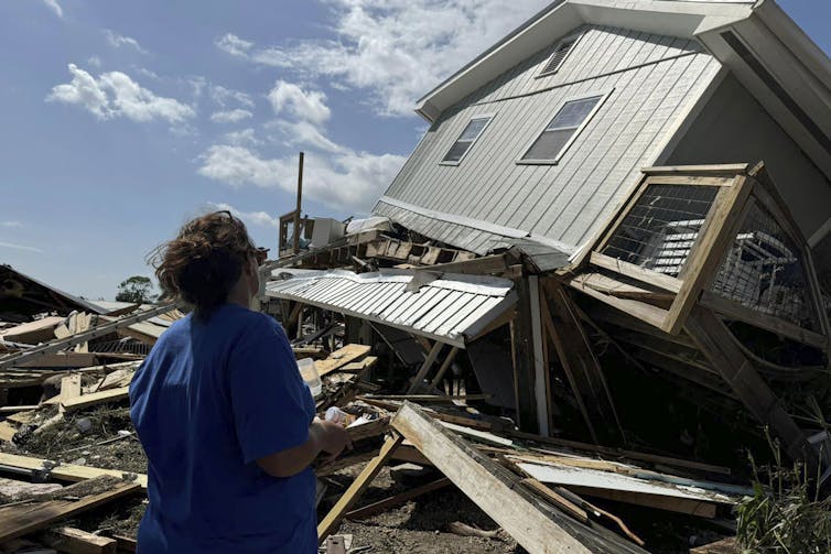 Woman looks on at her house, which was lifted up and on its side at an angle by the storm, with debris everywhere