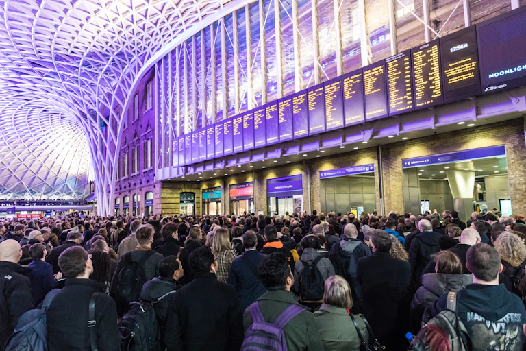 crowds of people staring up at a railway station departures board