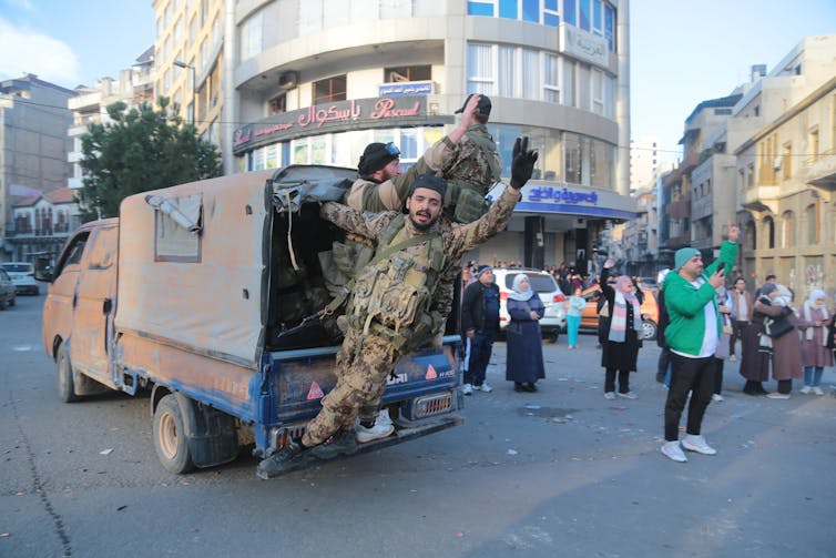 Men hand out of a car saluting to a nearby crowd.