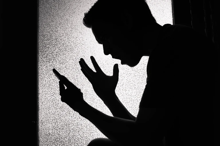 Silhouette of upset young man looking at his smartphone screen.