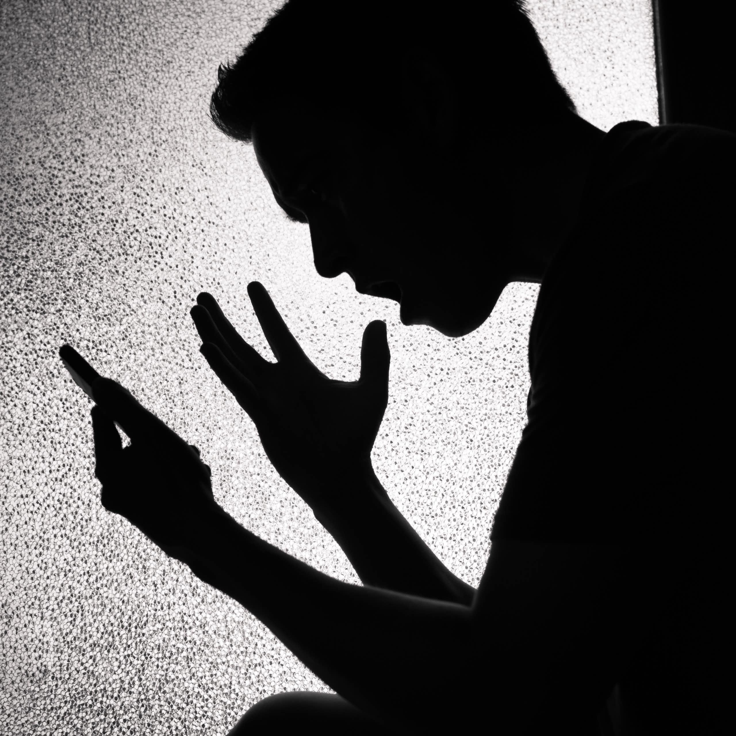 Silhouette of upset young man looking at his smartphone screen.